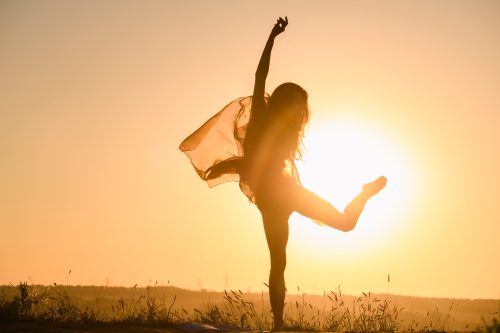 Dancing girl silhouette in warm sun light with transparent cloth, female fit body curves, activity outdoors